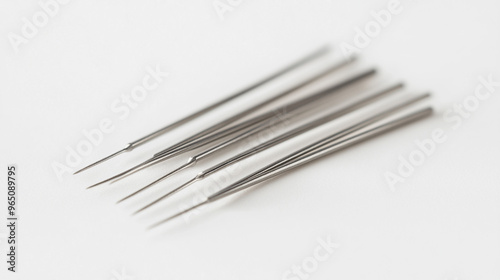 Set of six stainless steel sewing needles on a light background showcasing their sharp points and slender design