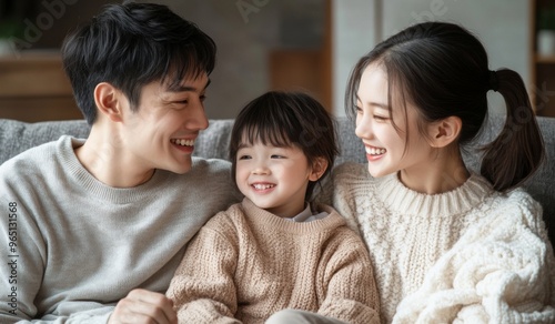 A happy Chinese family with two children sitting on the sofa at home, laughing and playing together in the living room. High-quality, realistic photograph.