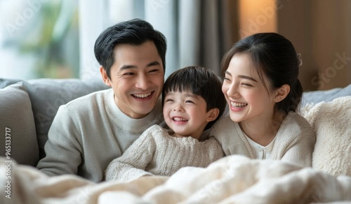 A happy Chinese family with two children sitting on the sofa at home, laughing and playing together in the living room. High-quality, realistic photograph.