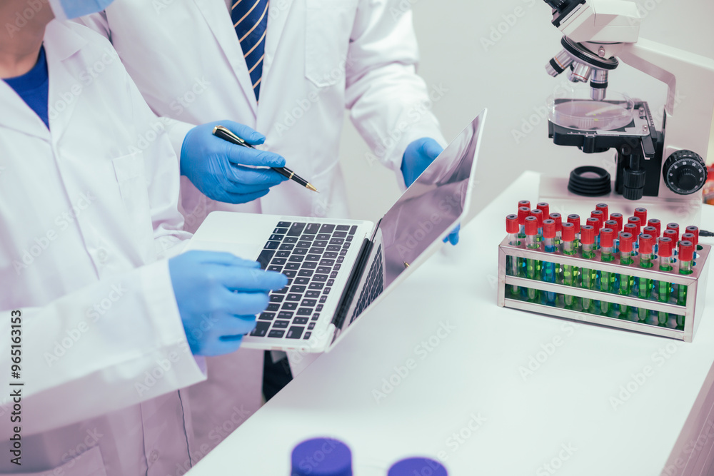 Two male researchers are conducting chemical research in a science lab, carefully analyzing substances at a desk filled with scientific instruments and chemical solutions in a well-organized Two male researchers are conducting chemical research in a science lab, carefully analyzing substances at a desk filled with scientific instruments and chemical solutions in a well-organized