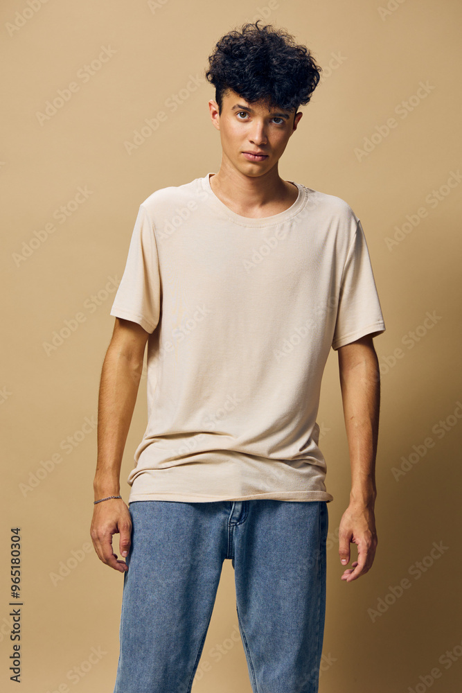 Casual fashion portrait of a young man wearing a beige t shirt and blue jeans against a warm beige background, representing contemporary style and youth culture Casual fashion portrait of a young man wearing a beige t shirt and blue jeans against a warm beige background, representing contemporary style and youth culture