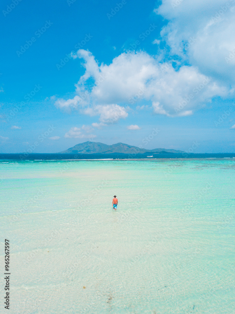 Aerial view of man stands on the white sand by the beach with clear blue ocean water. summer background and summer holiday concept