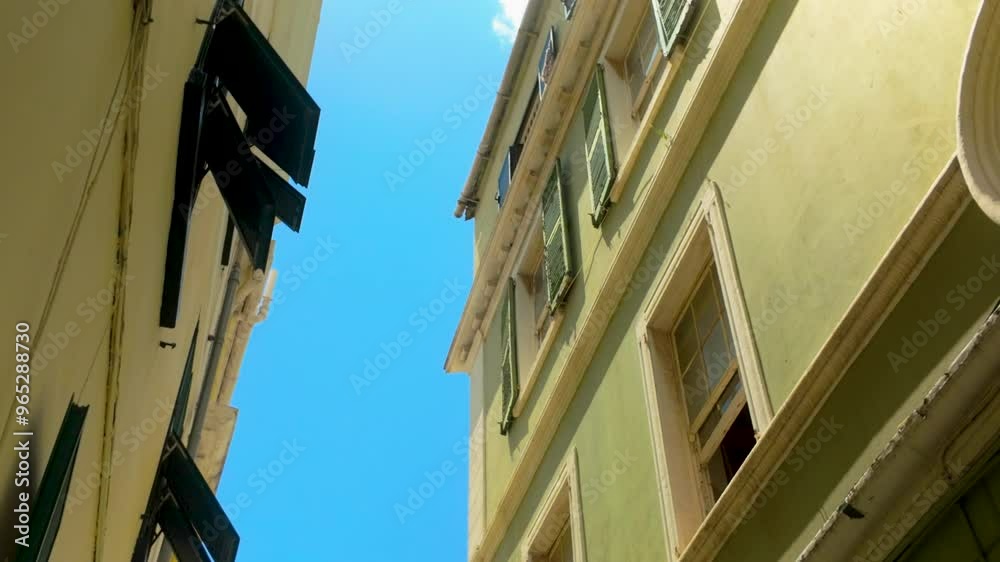 Upward view of a narrow alleyway flanked by historic buildings, showcasing traditional European architecture under a clear sky