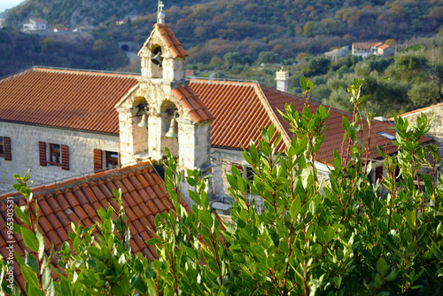 Landscape from the Gradiste Monastery, built in the outskirts of Budva: green foliage of the laurel and the belfry of the Church of St. Nicholas against the background of the monastery building photo