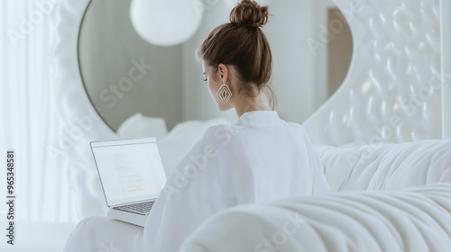A woman works on her laptop in a minimalist white workspace that fosters calmness and creativity