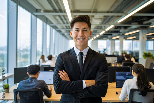 Young Asian Businessman in Modern Office, Smiling in Formal Attire, Background contain employees working at their desks, Corporate Work Environment