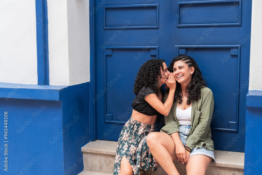 Two young women sharing a secret while sitting on steps. Two young women sharing a secret while sitting on steps.