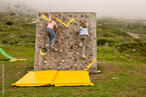 Girls climbing a wall  in mountain outdoors playground. Kids, childrens activity in Trentino mountains. Mountain top of the Adamello Brenta national park in a foggy day, Italy. No visible faces. photo