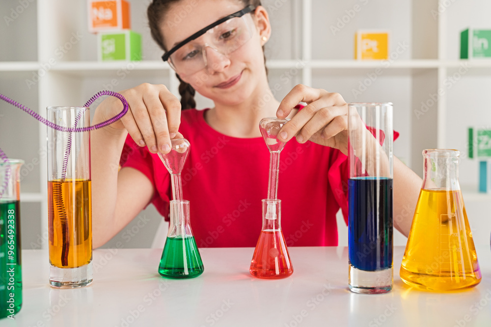 Young girl wearing safety goggles conducting a science experiment with colorful liquids in a laboratory setting. Young girl wearing safety goggles conducting a science experiment with colorful liquids in a laboratory setting.