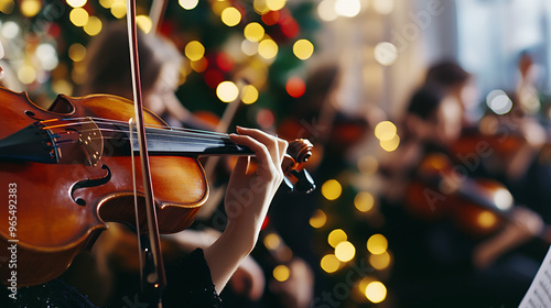 Close-up of a violin being played in front of a Christmas tree with warm holiday lights, creating a festive and joyful atmosphere perfect for a Christmas concert or celebration