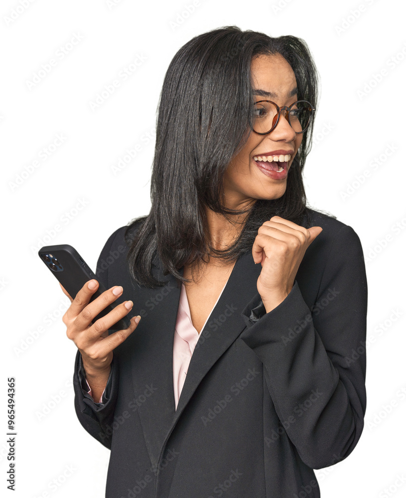 Latina in suit with phone in studio points with thumb finger away, laughing and carefree. Latina in suit with phone in studio points with thumb finger away, laughing and carefree.