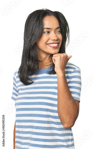 Young Latina posing in studio points with thumb finger away, laughing and carefree.