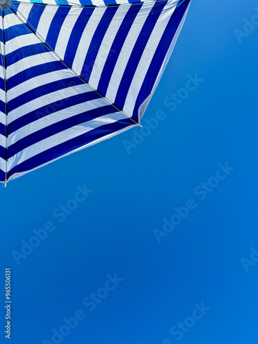 Fragment of white and blue striped beach umbrella close up against clear blue sky with text space