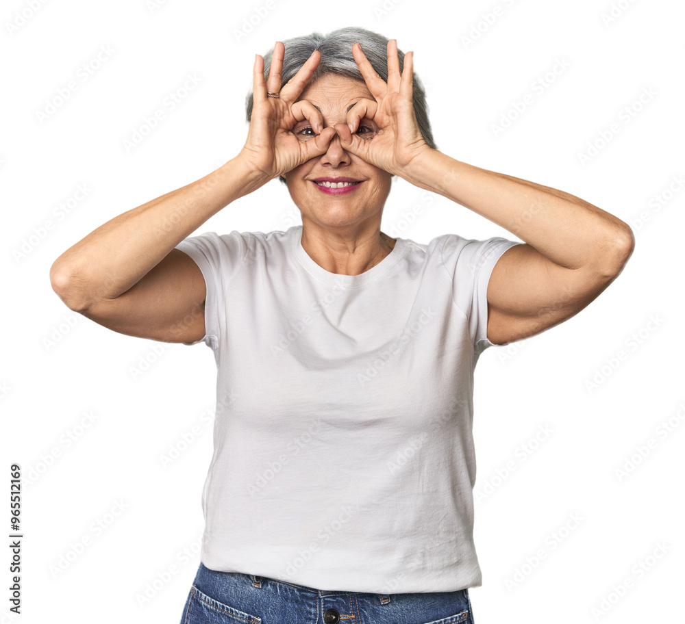 Caucasian mid-age female on studio background showing okay sign over eyes Caucasian mid-age female on studio background showing okay sign over eyes
