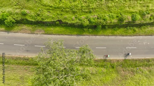 two cyclists couple ride bicycles on road in nature surrounded by greenery. Friends on bikes ride together have fun outdoors. Aerial drone top down bird eye view shot of beautiful epic green land