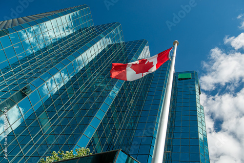 Obraz na plátne Canadian Flag waves in front of a building in Ottawa, clouds and blue sky reflections on the building windows