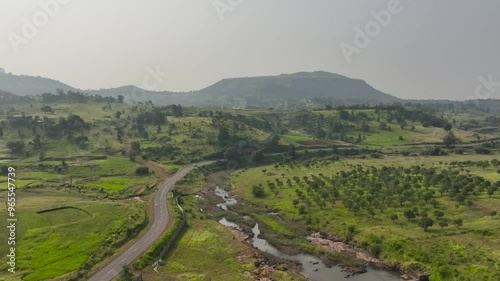 wide aerial view Car Driving on Country Road. vehicle riding fast along fields mountains. Cinematic drone shot flying over gravel road with trees