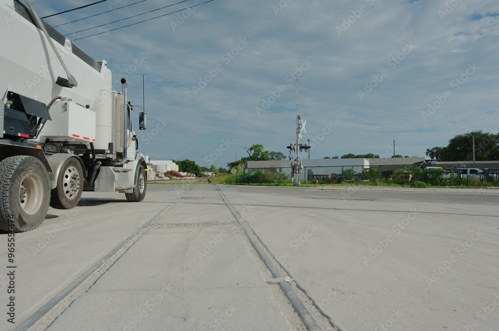 Leading lines of Side view Railroad tracks of a large white cement truck late afternoon with blue sky and white clouds in back.Railroad tracks in front dusty road with building block and train signal Leading lines of Side view Railroad tracks of a large white cement truck late afternoon with blue sky and white clouds in back.Railroad tracks in front dusty road with building block and train signal