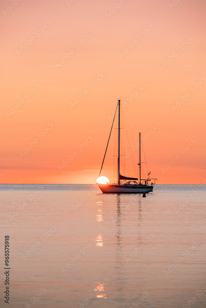 Sailboat Over The Horizon At Sunrise. Moored On Calm Waters, With The Sun Rising On The Horizon, With An Orange Glow In The Sky And Reflections On The Water Of The Mediterranean. Collioure (Cotlliure)