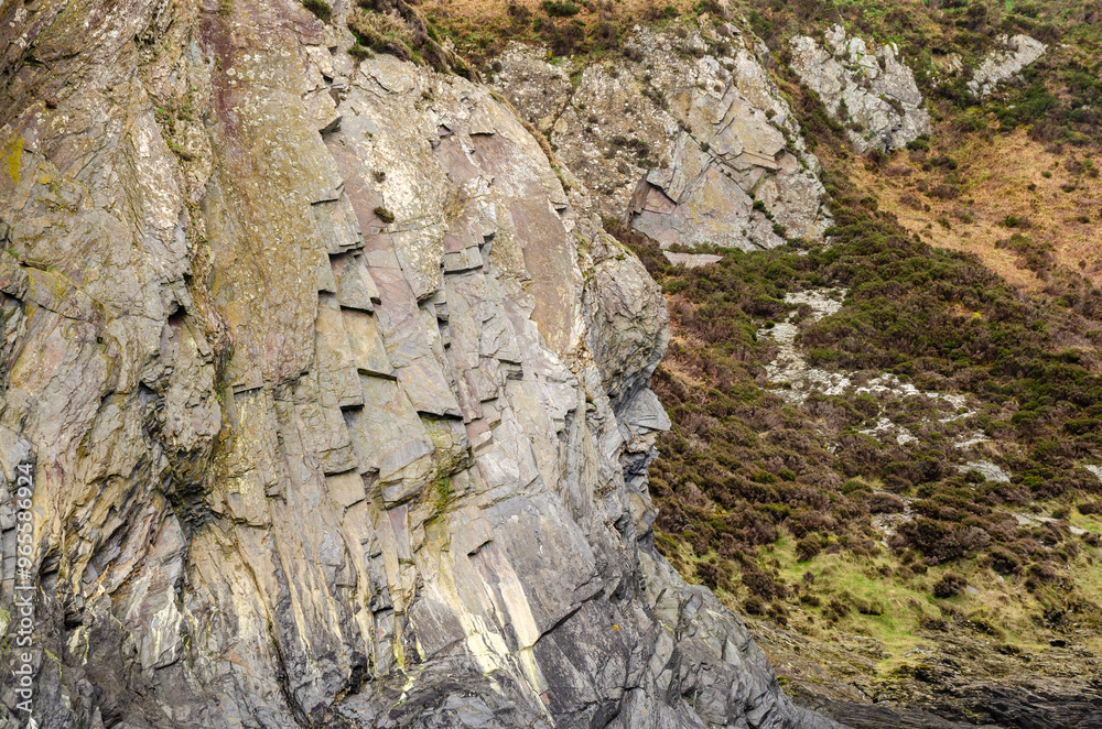 Close-up of a rocky cliff face with vegetation growing on top. Close-up of a rocky cliff face with vegetation growing on top.
