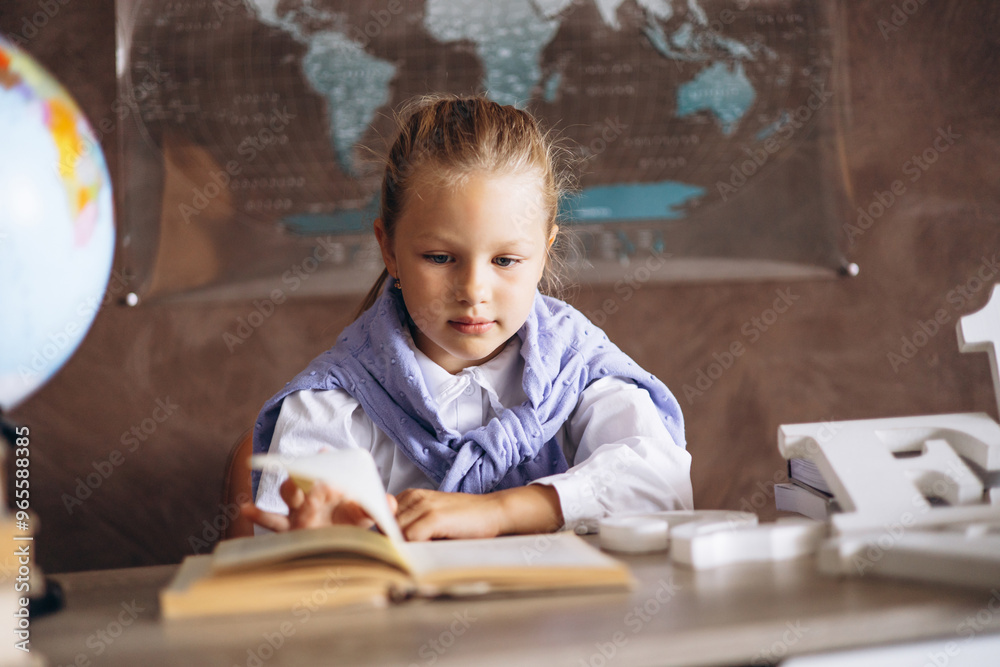 Little schoolgirl sitting at the desk in classroom and writing in notebook Little schoolgirl sitting at the desk in classroom and writing in notebook