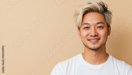 portrait of asian softly smiling young man with blond hair on light beige color background, copy space, student,
