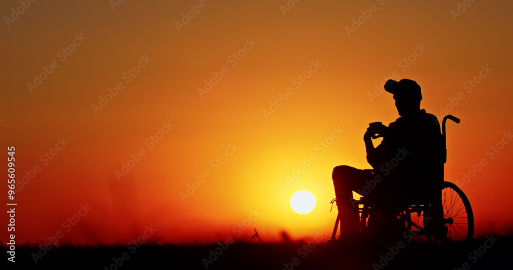 Silhouette of a man in a wheelchair at sunset with a vibrant orange sky. Silhouette of a man in a wheelchair at sunset with a vibrant orange sky.