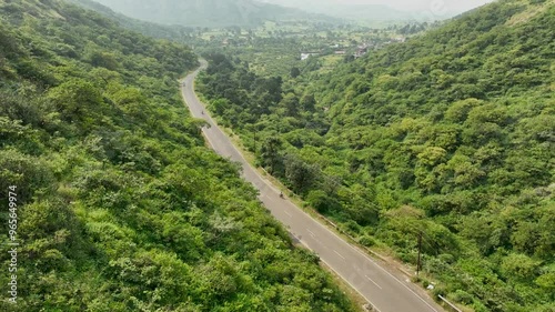 single cyclist ride bicycle on road in nature surrounded by mountains greenery. adult bike riding having fun in nature outdoors. wide cinematic aerial drone shot of beautiful epic green landscape.