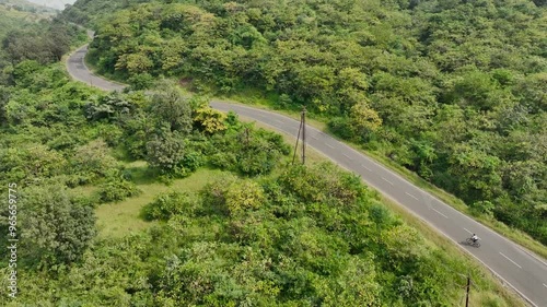single cyclist ride bicycle on road in nature surrounded by mountains greenery. women bike riding having fun outdoors. Aerial drone shot of beautiful scenic landscape.