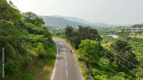 single cyclist ride bicycle on road in nature surrounded by mountains greenery. women bike riding having fun in nature outdoors. wide aerial drone shot of beautiful epic green landscape.