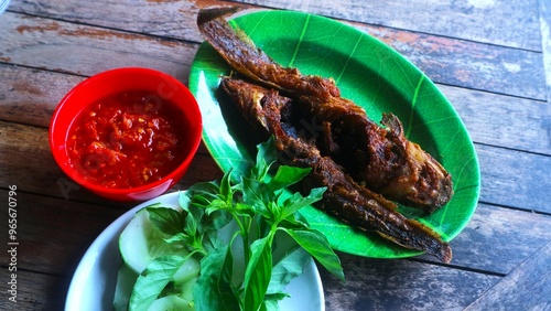 Pecel lele, traditional Indonesian food fried lele served with aromatic kemangi leaf and chili sauces on wooden table photo