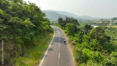 single cyclist ride bicycle on road in nature surrounded by mountains greenery. women bike riding having fun in nature outdoors. wide aerial drone shot of beautiful epic green landscape.
