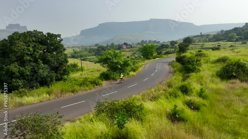 single cyclist ride bicycle on road in nature surrounded by mountains greenery river. adult bike riding having fun outdoors. Aerial drone shot of beautiful epic landscape.
