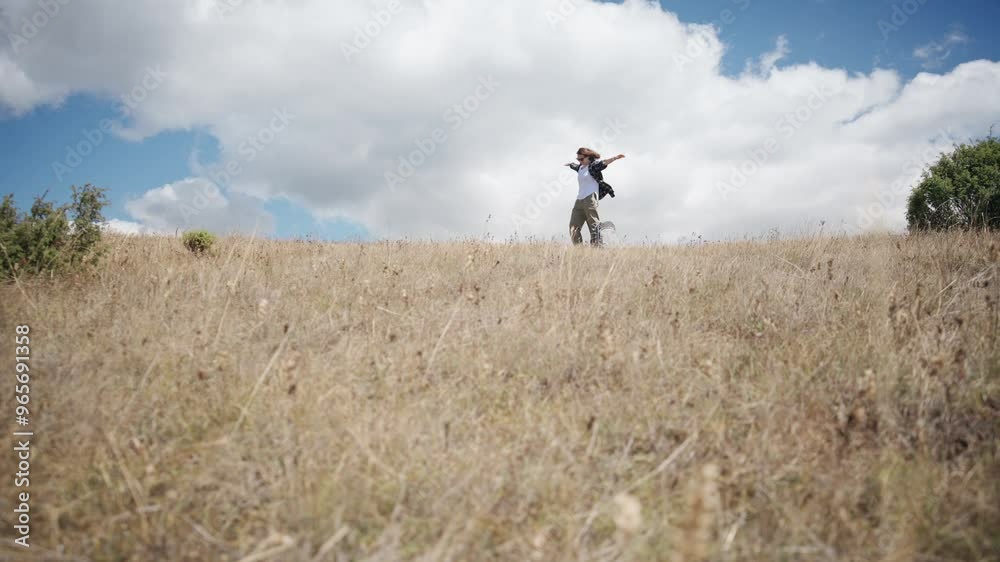 A young female traveler stands on top of a hill with her arms outstretched on a sunny day A young female traveler stands on top of a hill with her arms outstretched on a sunny day