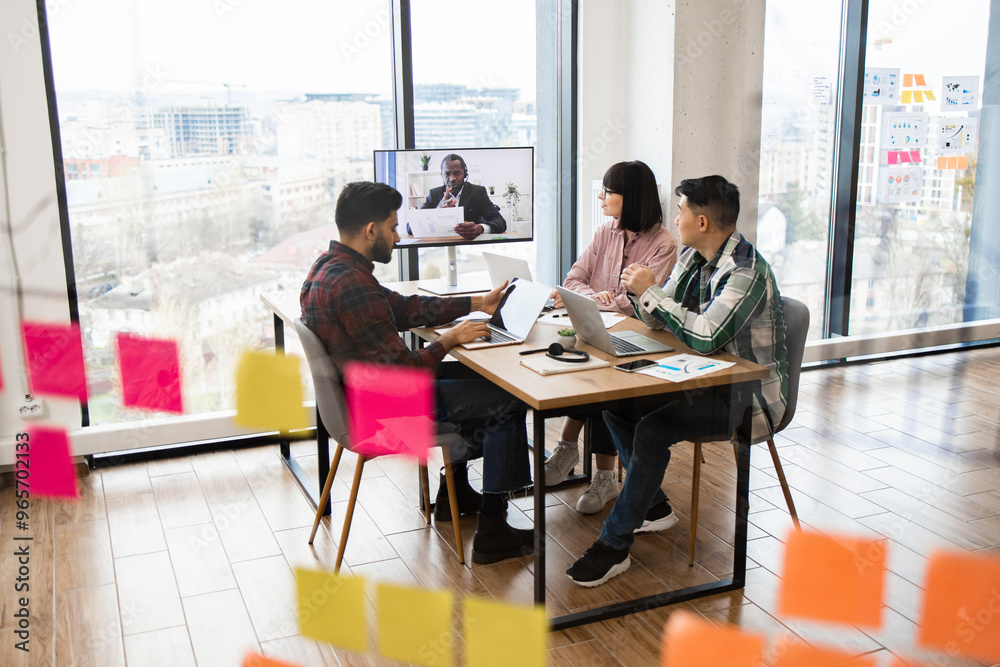 Office setting where team collaborates on project through brainstorming session and video conference call. Large windows and sticky notes create modern, productive environment. Office setting where team collaborates on project through brainstorming session and video conference call. Large windows and sticky notes create modern, productive environment.