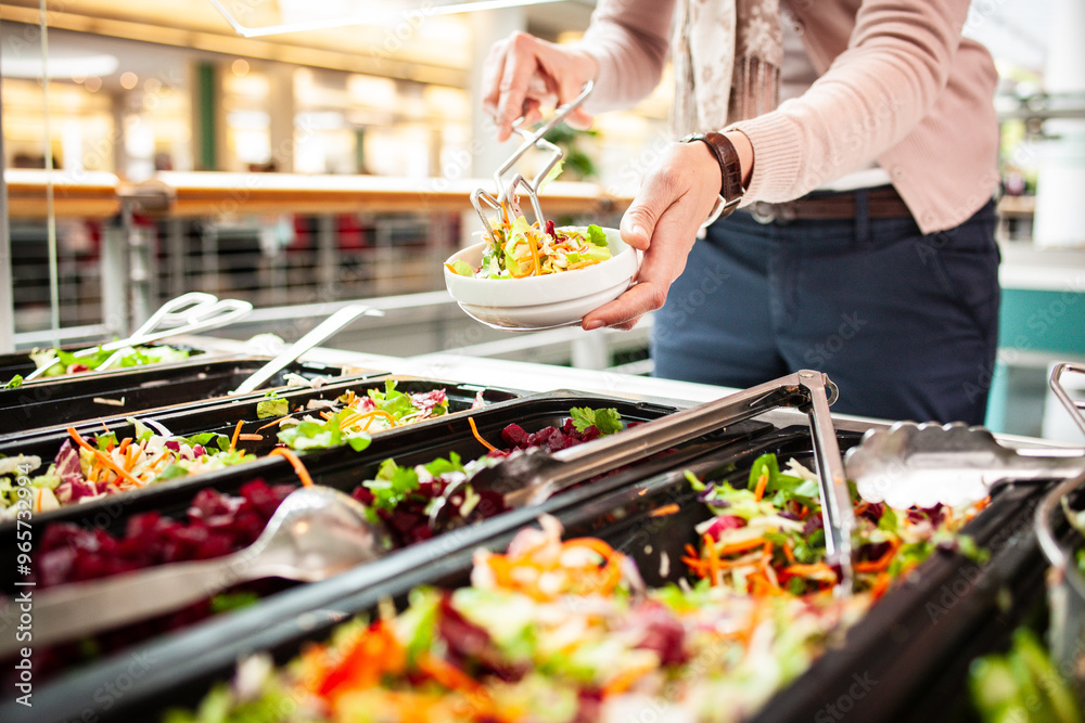 Fototapeta premium Frische Salate in einem Salatbuffet, eine Frau bedient sich am Buffet