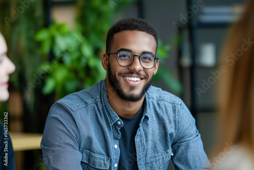 Handsome young African American guy wearing denim shirt and eyeglasses smiling job interview or talking with colleagues in the office.