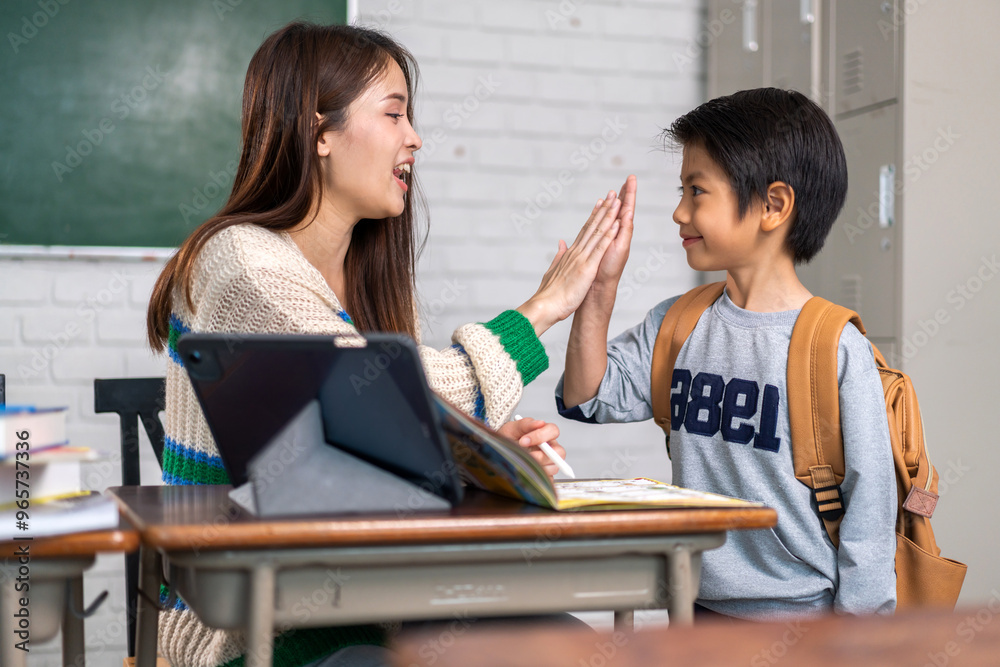 Asian teacher giving high five to young student in classroom, education and learning concept, smiling teacher and child, school environment, interactive learning, back to school, student encouragement Asian teacher giving high five to young student in classroom, education and learning concept, smiling teacher and child, school environment, interactive learning, back to school, student encouragement