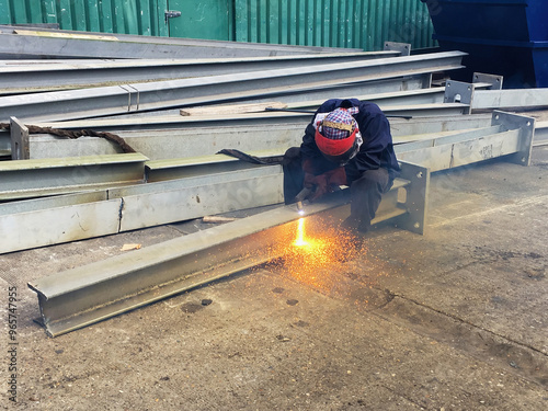 A worker using an electric plasma cutter to reduce the size of a steel girder photo