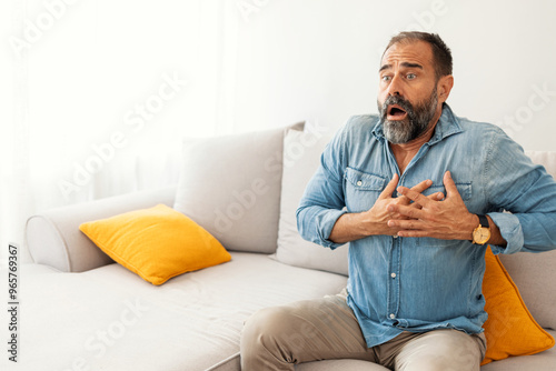 Shocked Mature Man Sitting on Sofa with Hands on Chest