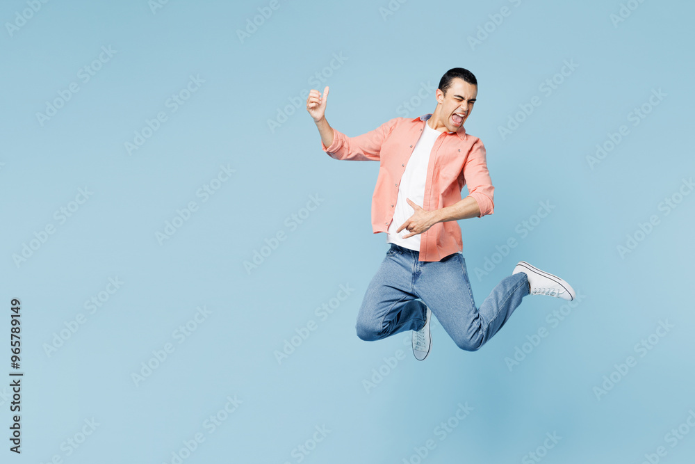 Full body young musician middle eastern man he wear pink shirt white t-shirt jump high play imaginary air guitar isolated on plain pastel light blue cyan background studio portrait. Lifestyle concept. Full body young musician middle eastern man he wear pink shirt white t-shirt jump high play imaginary air guitar isolated on plain pastel light blue cyan background studio portrait. Lifestyle concept.
