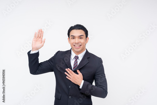 A young asian business executive swearing an oath and placing his hand in his chest, promising to be truthful. Isolated on a white background.