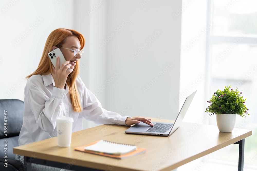 Woman entrepreneur making notes and talking by phone with client while sitting in office Woman entrepreneur making notes and talking by phone with client while sitting in office