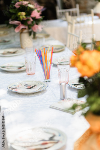 Elegant outdoor dining setup with colorful straws and fresh flowers for a summer gathering in a garden