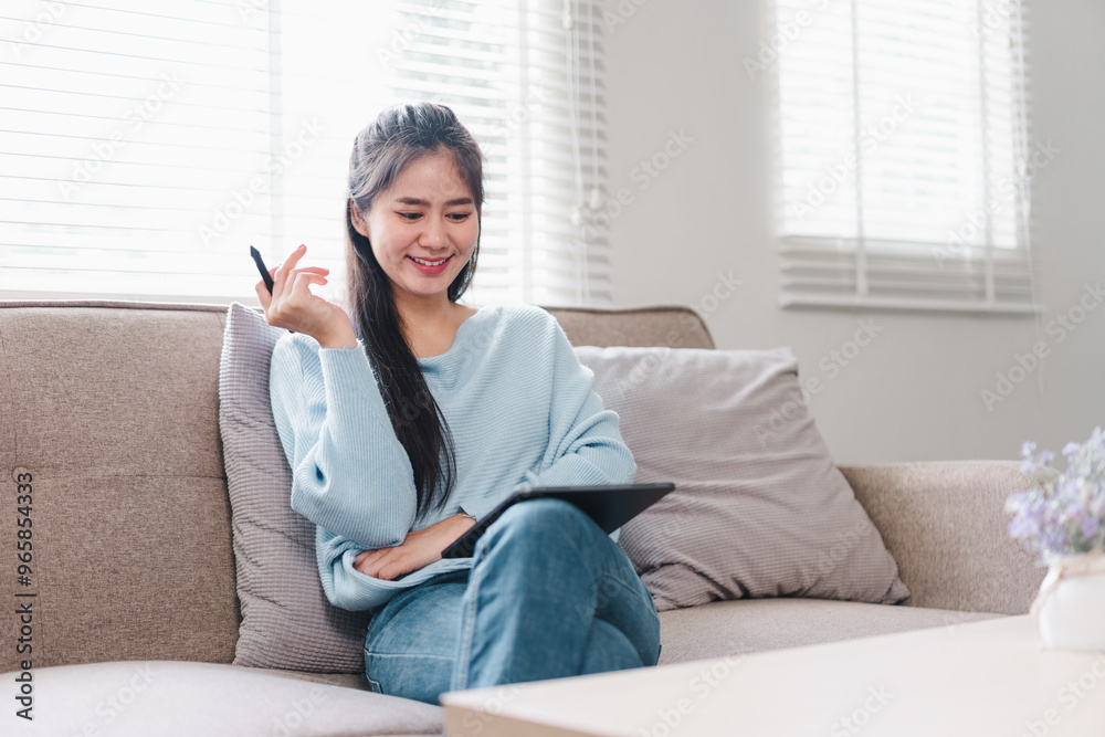 A young woman is sitting comfortably on sofa, smiling while using tablet. She appears relaxed and engaged, showcasing modern living space with natural light. A young woman is sitting comfortably on sofa, smiling while using tablet. She appears relaxed and engaged, showcasing modern living space with natural light.