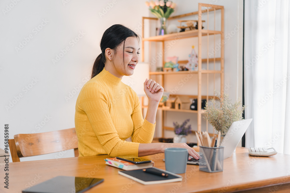A woman in yellow sweater is working on her laptop at wooden desk, surrounded by plants and stationery. cozy atmosphere enhances her focused expression. A woman in yellow sweater is working on her laptop at wooden desk, surrounded by plants and stationery. cozy atmosphere enhances her focused expression.