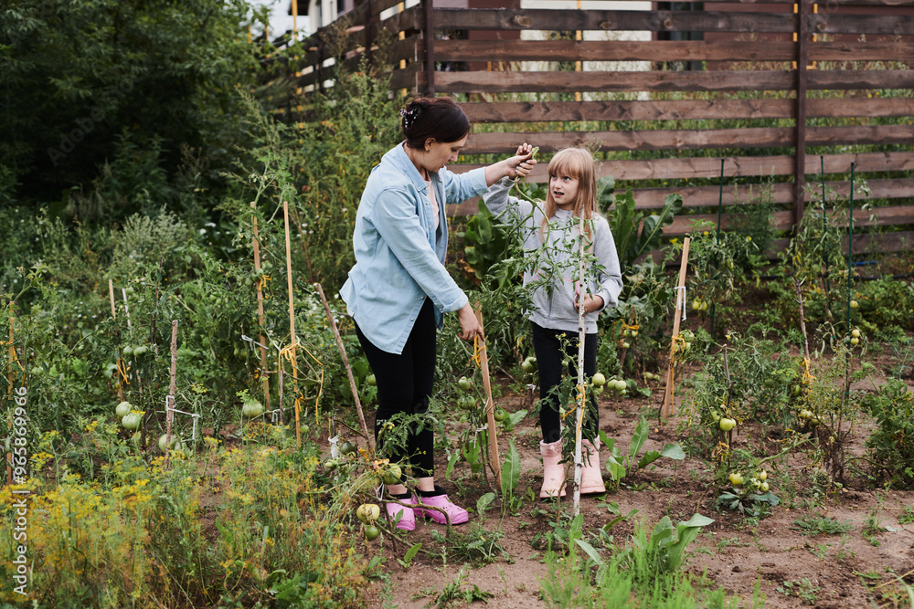 Little girl helping her mother work in the garden in the backyard of the house Little girl helping her mother work in the garden in the backyard of the house