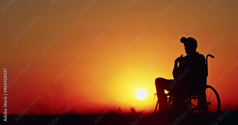 Silhouette of a man in a wheelchair at sunset with a vibrant orange sky. Silhouette of a man in a wheelchair at sunset with a vibrant orange sky.