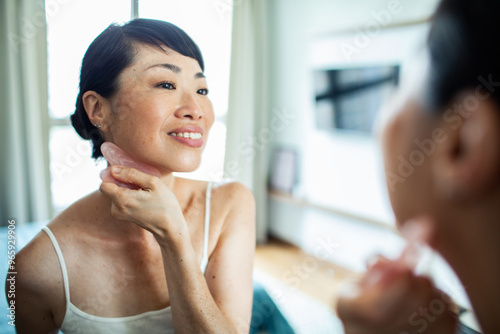 Asian woman using gua sha stone for facial skincare routine at home photo