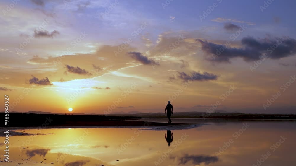 Man stands on lakeshore, admiring sunset over water. sky showcases vibrant hues of orange, yellow, and purple, while clouds mirror in lake calm surface Man stands on lakeshore, admiring sunset over water. sky showcases vibrant hues of orange, yellow, and purple, while clouds mirror in lake calm surface